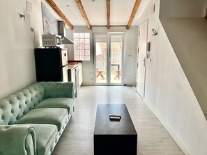 A modern loft with a green sofa, a black table, wooden beams, a kitchen, and a sliding glass door leading to an outdoor area. - Studio for couples with terrace on the beach (València)