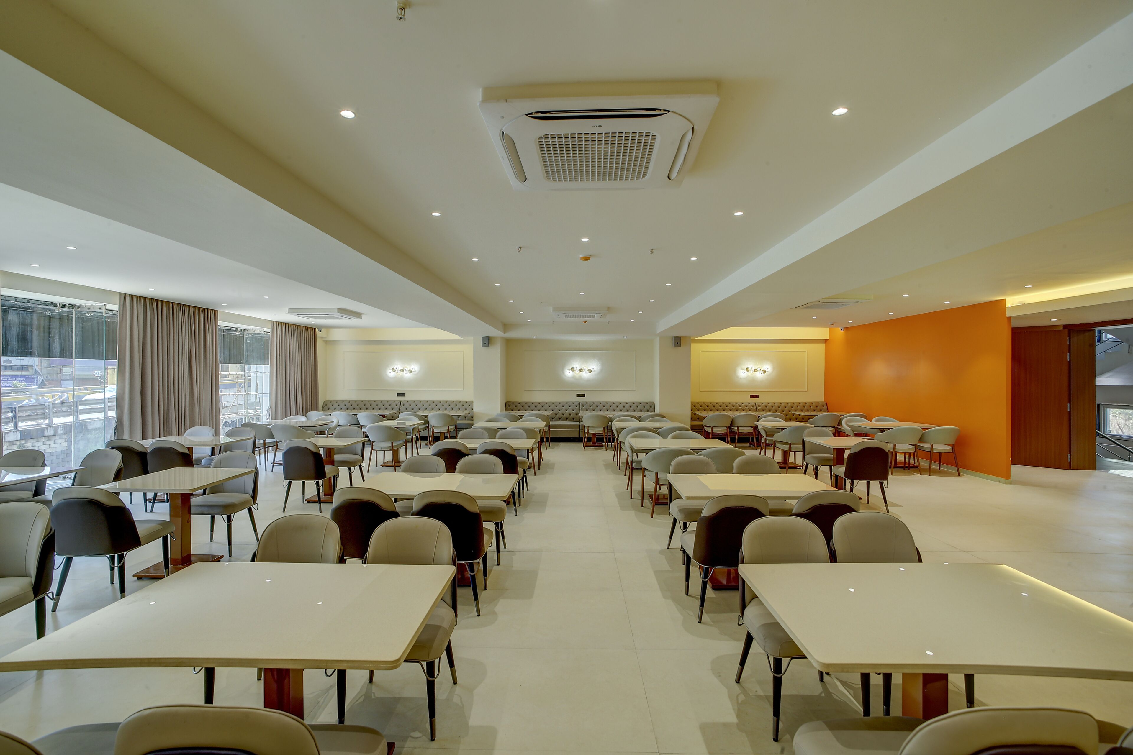 A spacious dining area with multiple tables and chairs, a large window, and an orange accent wall.