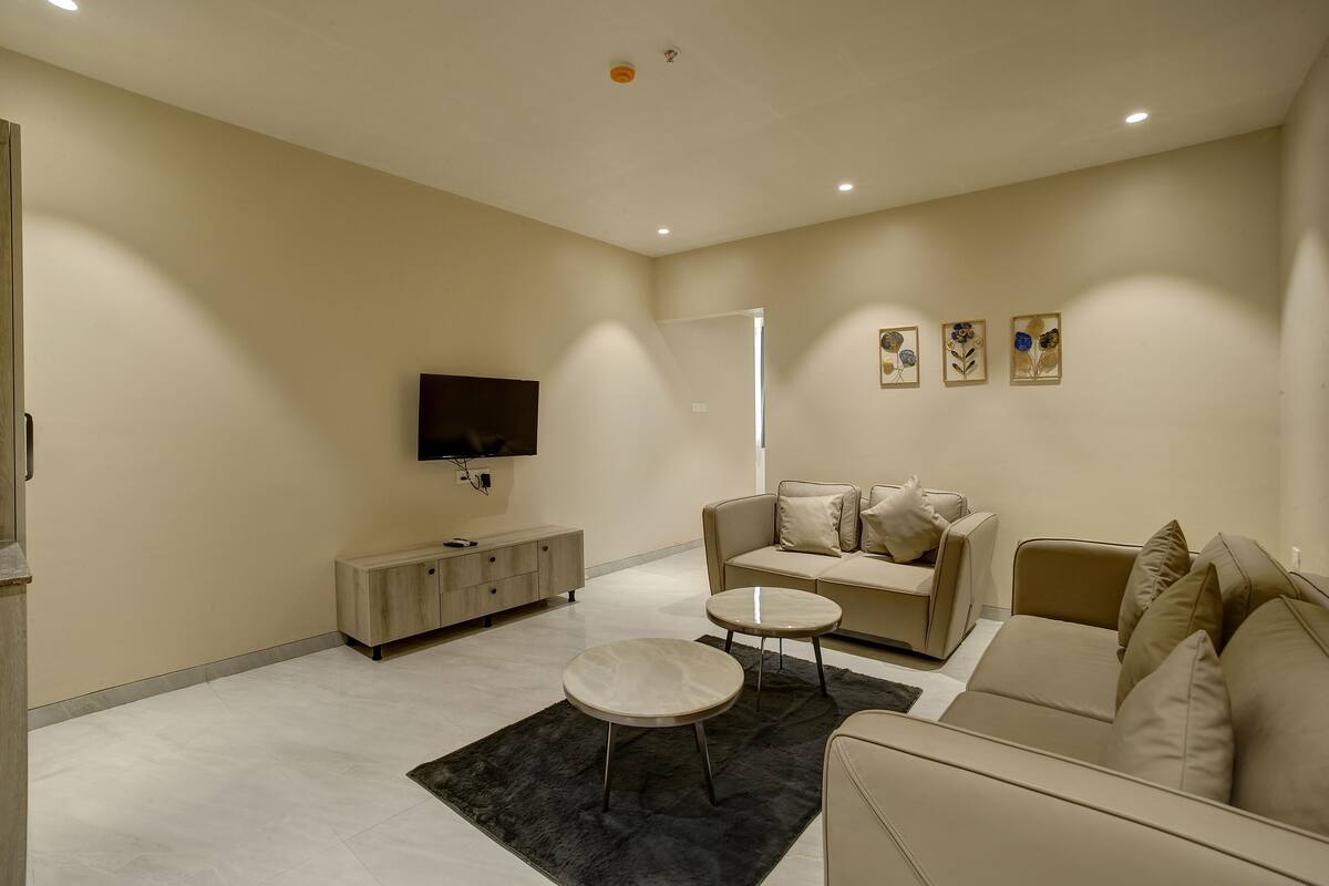 A modern living room with a sofa, two coffee tables, a TV, and artwork on the wall.