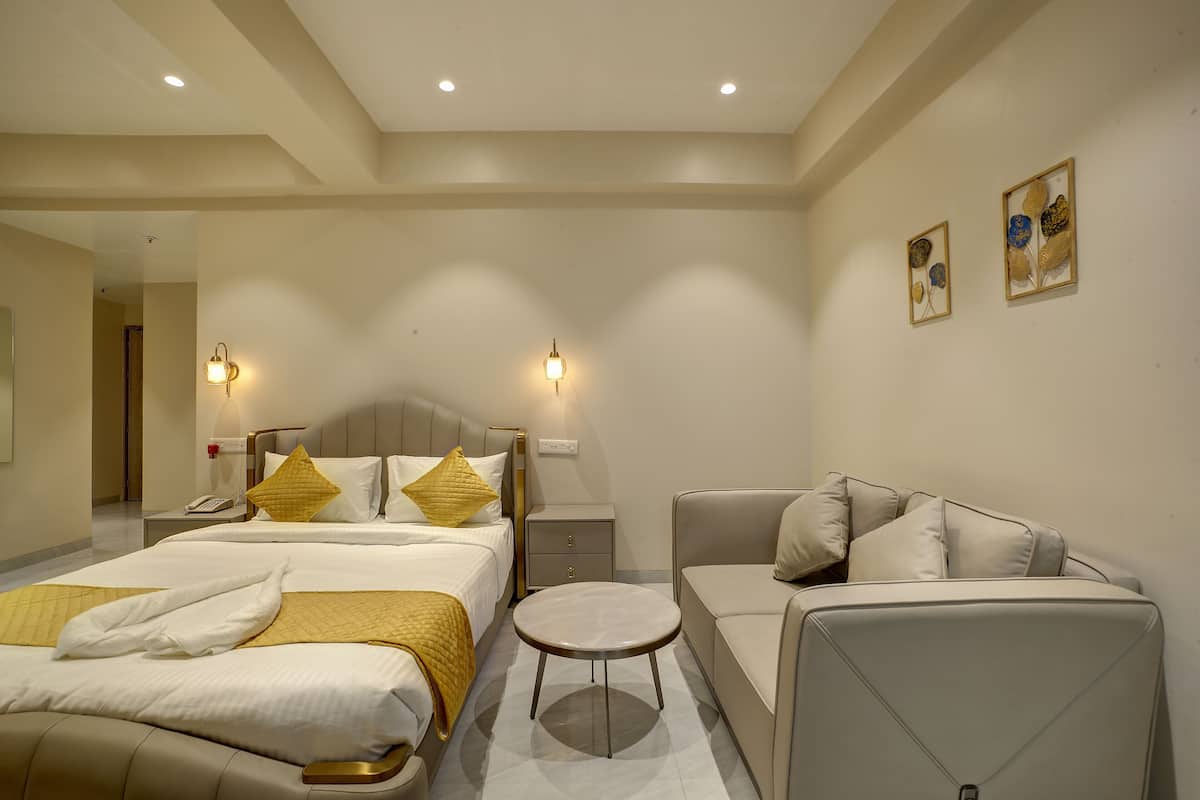 A hotel room with a bed, a sofa, a nightstand, a lamp, and artwork on the wall.