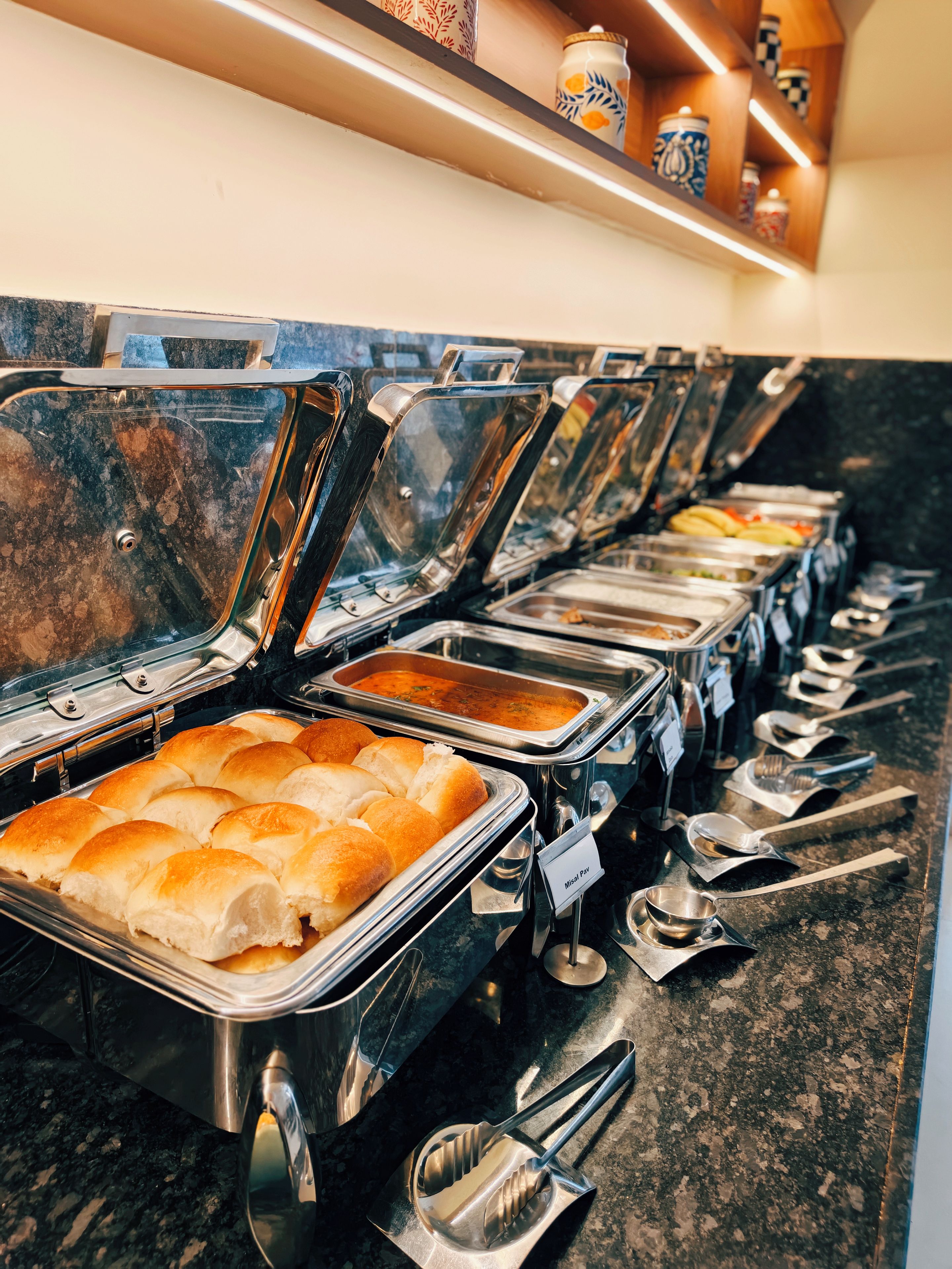 Una barra de buffet con diversas opciones de comida y utensilios de servicio.