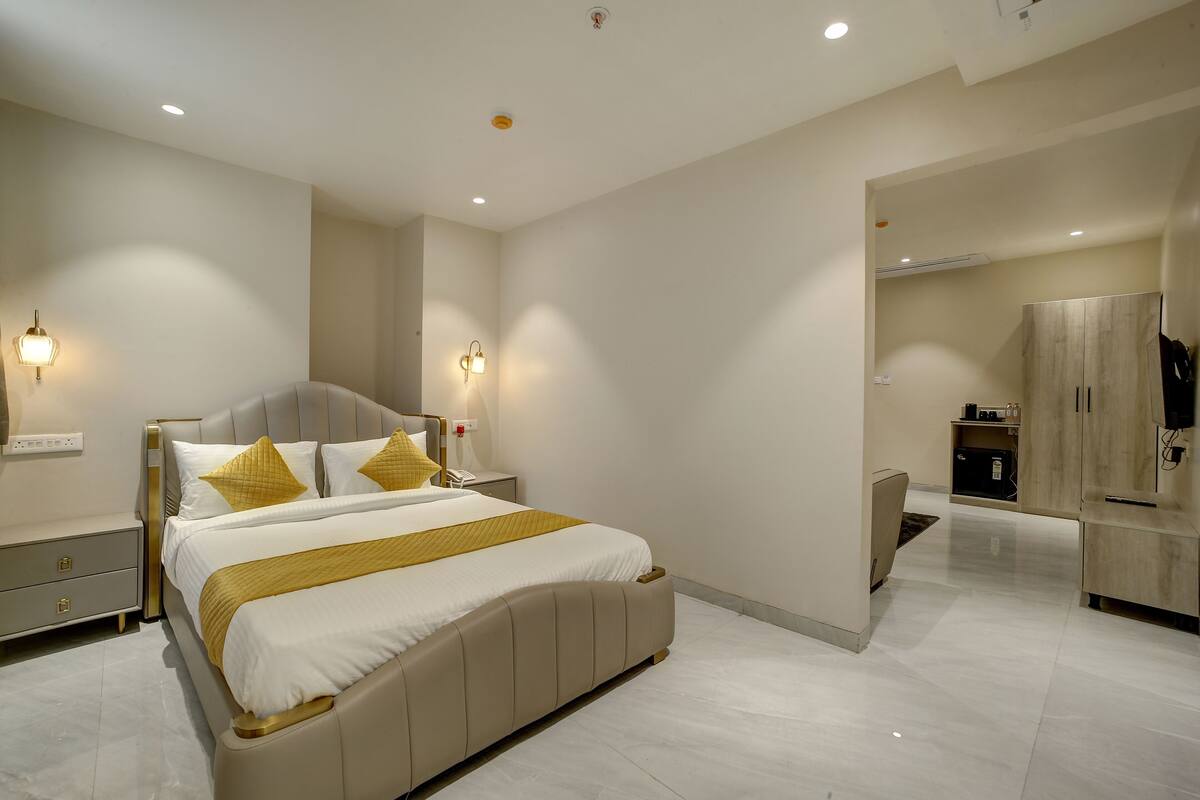 A modern bedroom with a large bed, bedside tables, a wardrobe, and a small kitchenette.