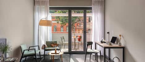 A hotel room with a bed, a desk, two chairs, a lamp, and a view of the outside.