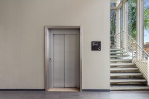 Ein moderner Aufzug mit geschlossener Tür, eine Treppe mit Metallgeländern und ein Schild mit der Angabe der Etage.