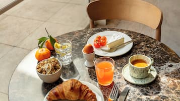 Desayuno con croissant, naranja y café sobre una mesa de mármol.