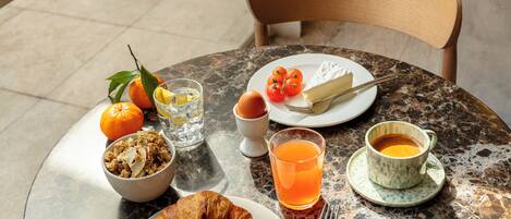 A breakfast setting with croissant, orange, and coffee on a marble table.