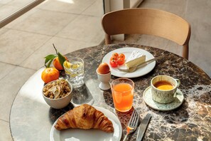 A breakfast setting with croissant, orange, and coffee on a marble table.