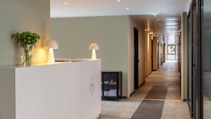 A hotel reception area with a reception desk, a potted plant, a lamp, and a glass door leading to the hallway. - Bob W Rome Testaccio (Rome)
