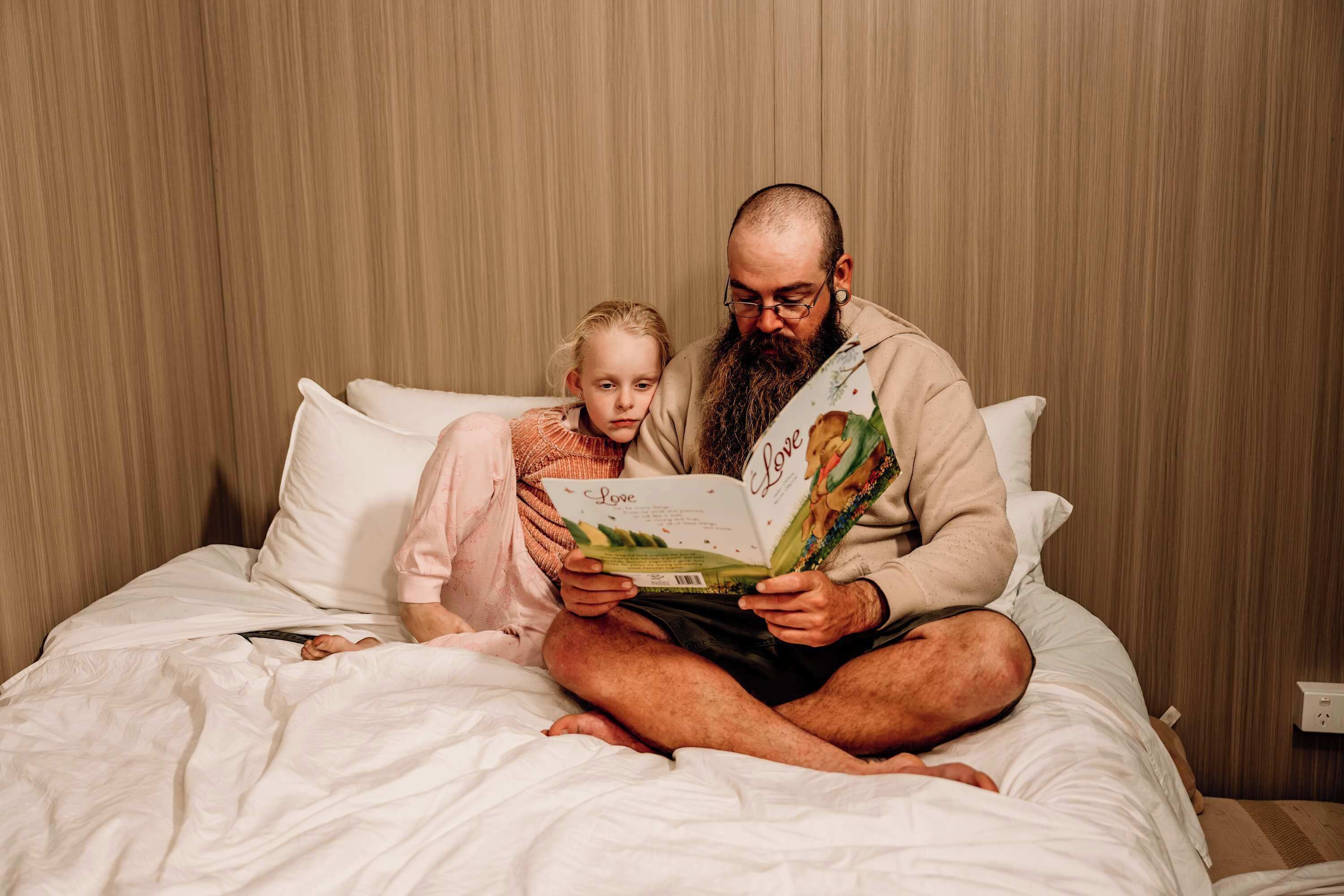 Un homme et un enfant sont assis sur un lit et lisent un livre.