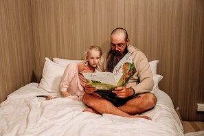 En mand og et barn sidder på sengen og læser en bog.