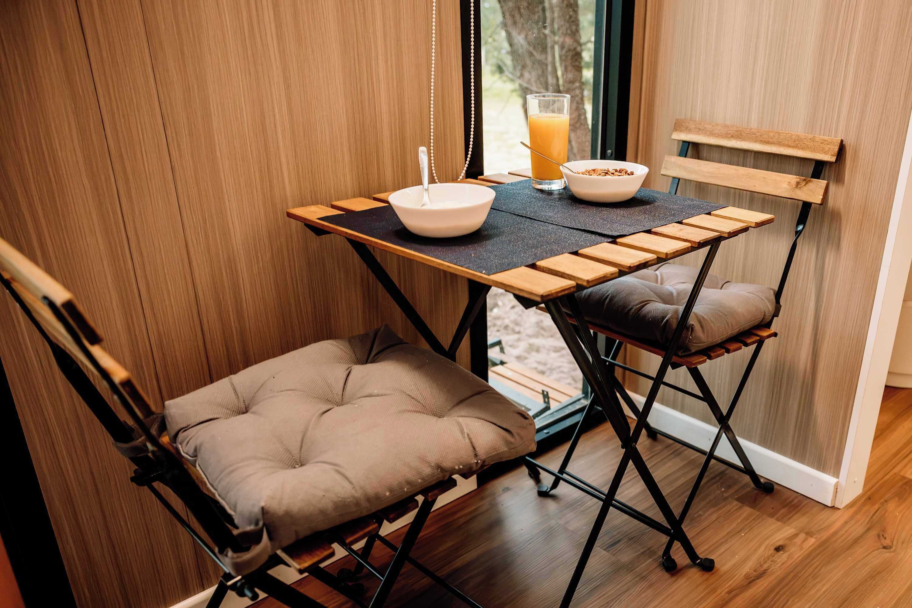 A compact dining area with a foldable table, two cushioned chairs, a bowl, a glass of orange juice, and a spoon.