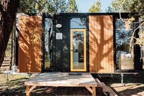 A compact, single-room cabin with a sliding door, a small porch, and a picnic table in front.
