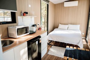 A compact room with a kitchenette, a bed, and a view of the outdoors.