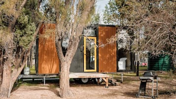 Une petite cabane en bois, dotée d’une porte et d’une fenêtre, entourée d’arbres.