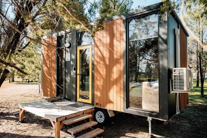 A small, modern mobile home with a wooden exterior, a sliding door, and a small porch with steps.