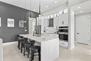 A modern kitchen with white cabinets, a marble island, and black bar stools. - Tiki Time! - Newly Listed (Cape Coral)