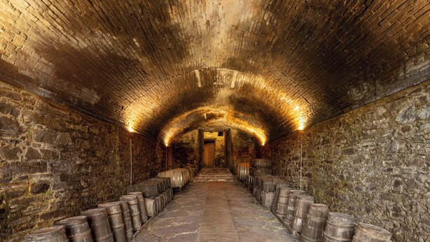 A stone-walled tunnel with barrels lined on either side and a central pathway leading to a door at the end. - Villa Bartolini Baldelli - Authentic XV century villa with garden and pool (Toscana)