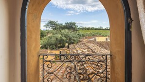 A view through an arched doorway with a wrought iron balcony railing, overlooking a terracotta-tiled roof and a green landscape with trees and buildings. - Villa Bartolini Baldelli - Authentic XV century villa with garden and pool (Toscana)