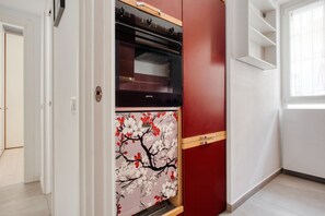 A kitchen with a built-in oven, a red cabinet, and a window with blinds. - Hostmate - Milano - Gessi - Washington (Milano)