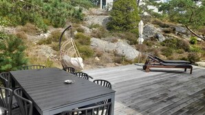 Une terrasse en bois avec une table et des chaises, un fauteuil suspendu et un fauteuil de relaxation.