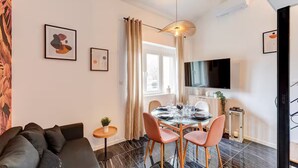 A modern living room with a sofa, a dining table with chairs, a TV, and artwork on the walls. - Lyon Est Élégance - Parking & Comfort (Meyzieu)