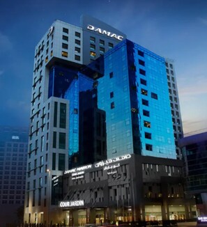 A high-rise hotel with "DAMAC" signage, "COUR JARDIN" branding, and a glass facade reflecting the sky. - Executive stay with hotel facilities (Dubai)