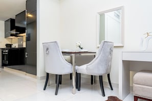 A modern kitchen with dark cabinets and a white countertop. There is a dining area with two white chairs and a small table. - Executive stay with hotel facilities (Dubai)
