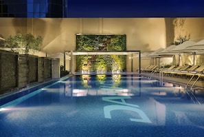 An indoor swimming pool with a tiled floor, a wall with a green vertical garden, and lounge chairs along the side. - Executive stay with hotel facilities (Dubai)