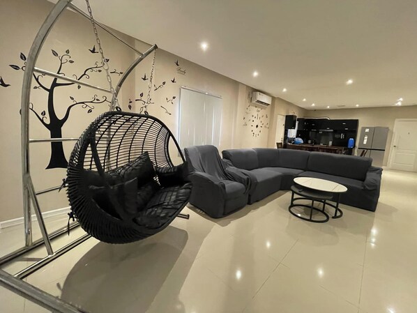 Uma sala moderna com um sofá seccional cinza, uma cadeira suspensa e uma pequena mesa redonda.