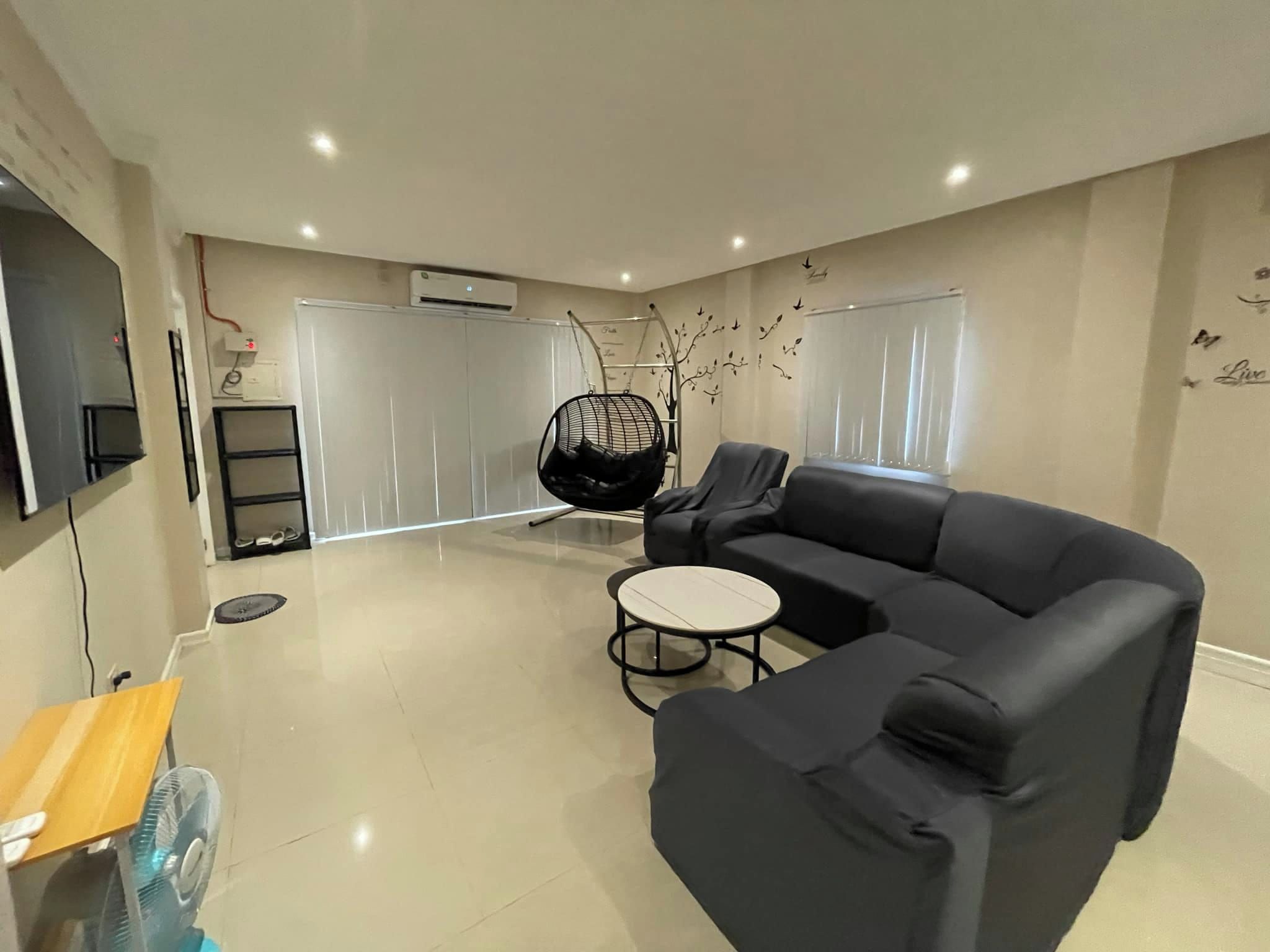 A modern living room with a black sofa, a hanging chair, a small table, and a TV mounted on the wall.