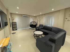 Uma sala de estar moderna com um sofá preto, uma cadeira suspensa, uma mesa pequena e uma televisão fixada na parede.
