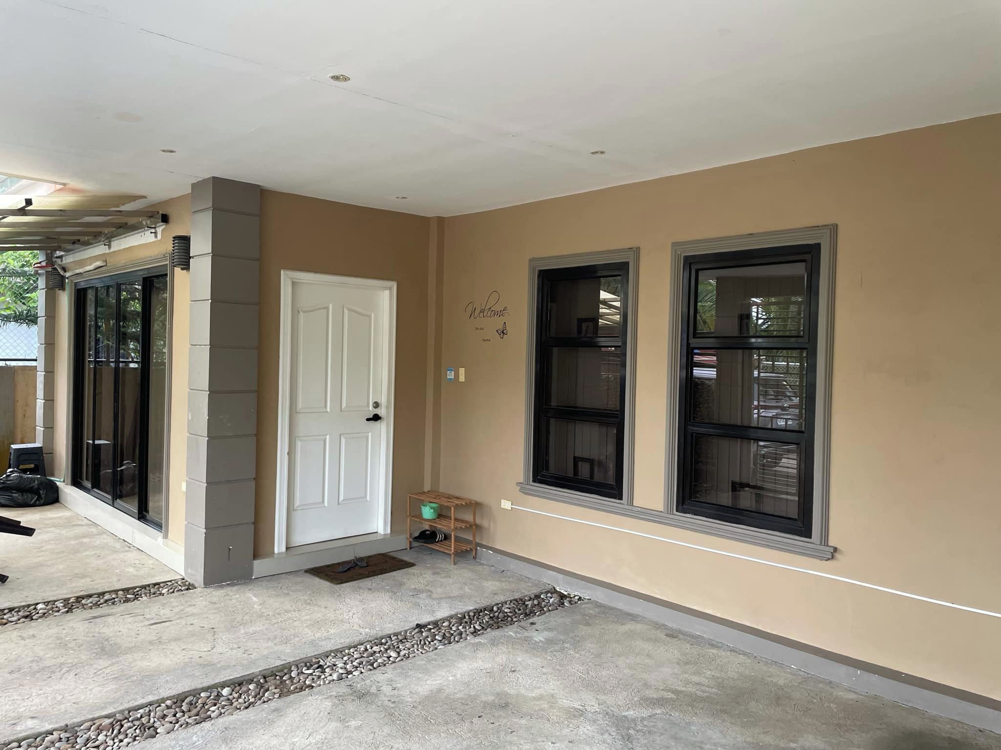 A house entrance with a beige exterior, a white door, and two windows with black frames.