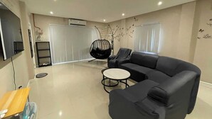 Een moderne woonkamer met een zwarte bank, een hangstoel, een bijzettafeltje en een aan de muur bevestigde televisie.