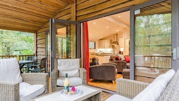 Una cabaña de madera con mobiliario de mimbre, un comedor y una cocina visible a través de puertas de vidrio.