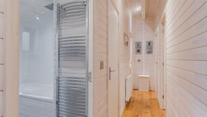 Un pasillo estrecho con paredes de madera y suelo de baldosas, que conduce a un baño con cabina de ducha de vidrio.