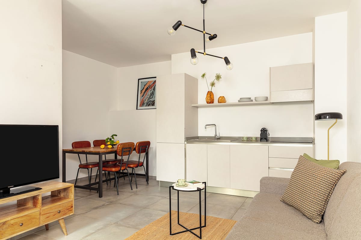 A modern living room with a flat-screen TV, a sofa, and a dining area with chairs and a table.