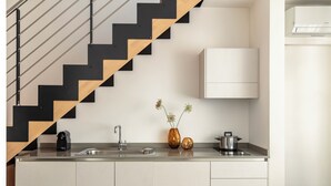 A modern kitchen with a stainless steel sink, a stove, and a built-in oven. There is a wooden staircase with black accents leading to another level.