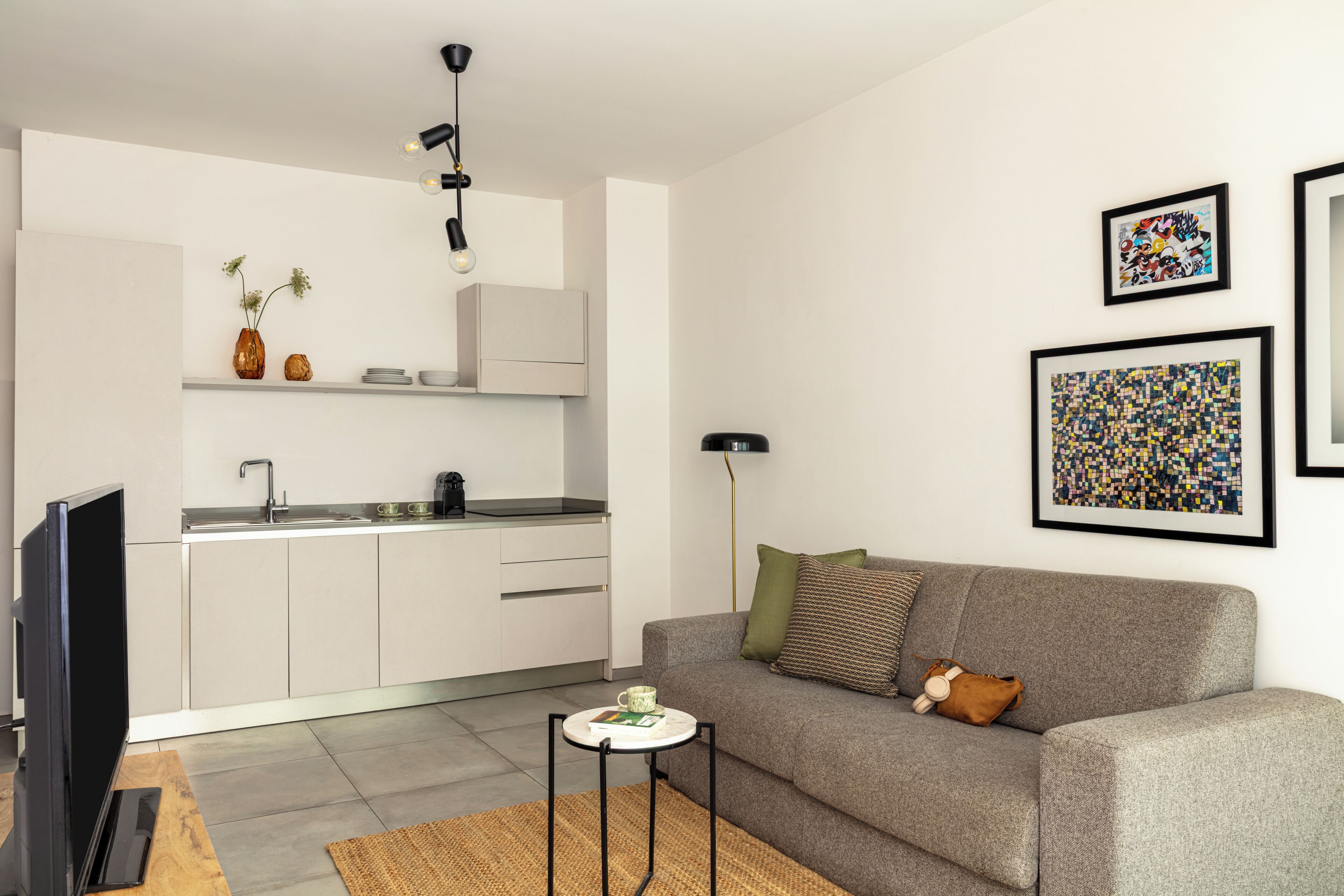 Uma sala de estar moderna com sofá, mesa de centro, TV, área de cozinha e obras de arte nas paredes.