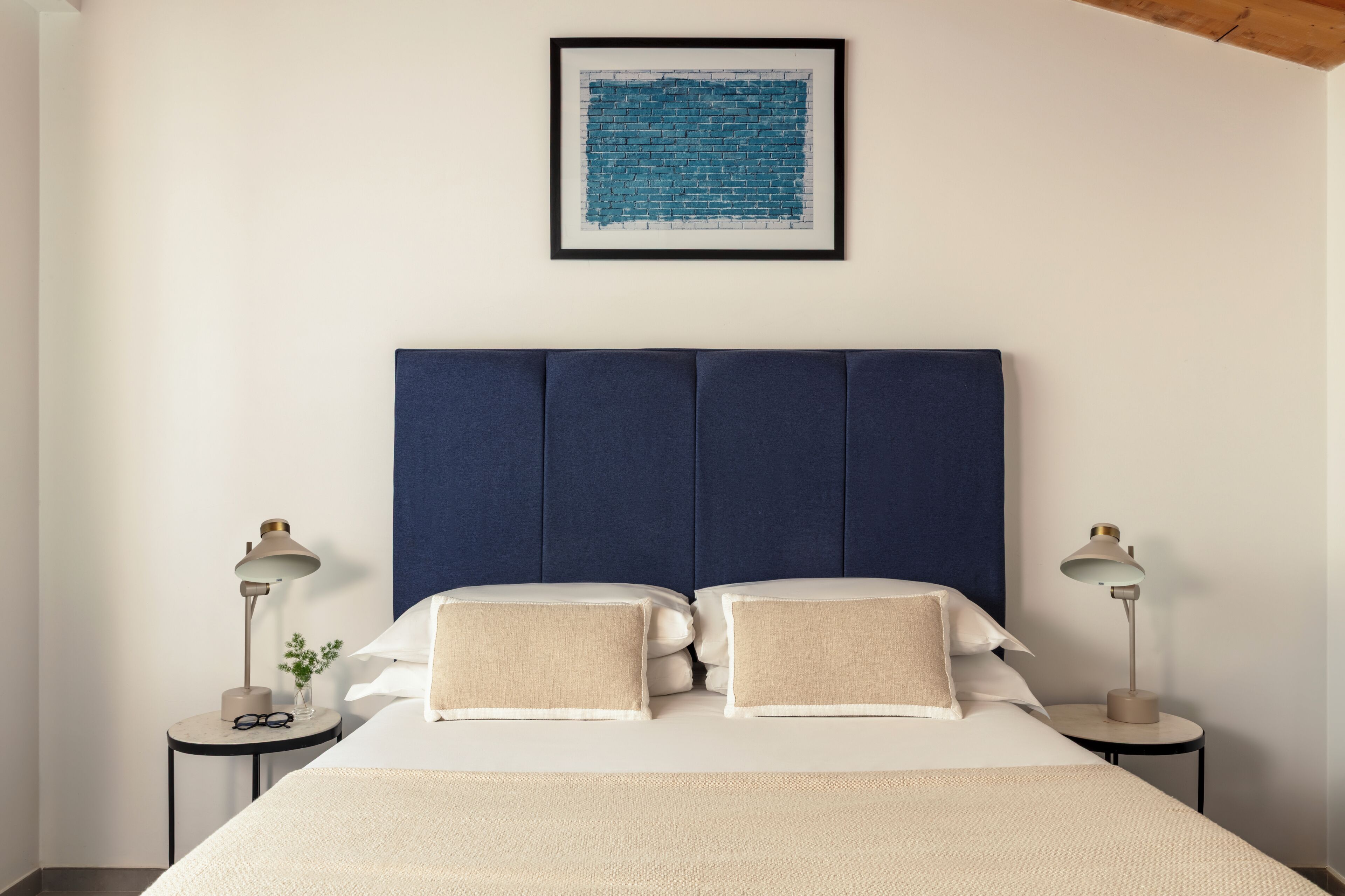 A neatly made bed with two pillows, a headboard, and two bedside tables with lamps.