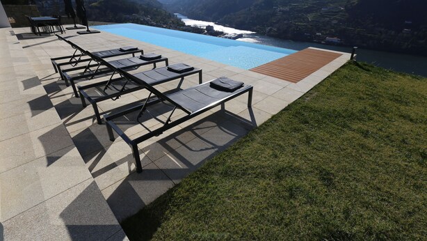 Un espace aménagé au bord de la piscine, avec des chaises longues et une terrasse en bois offrant une vue sur une rivière et des montagnes.