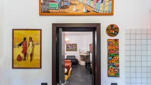 Un pasillo con un cuadro de una escena callejera, un comedor con una mesa y sillas, y una sala de estar con un sofá y un televisor.