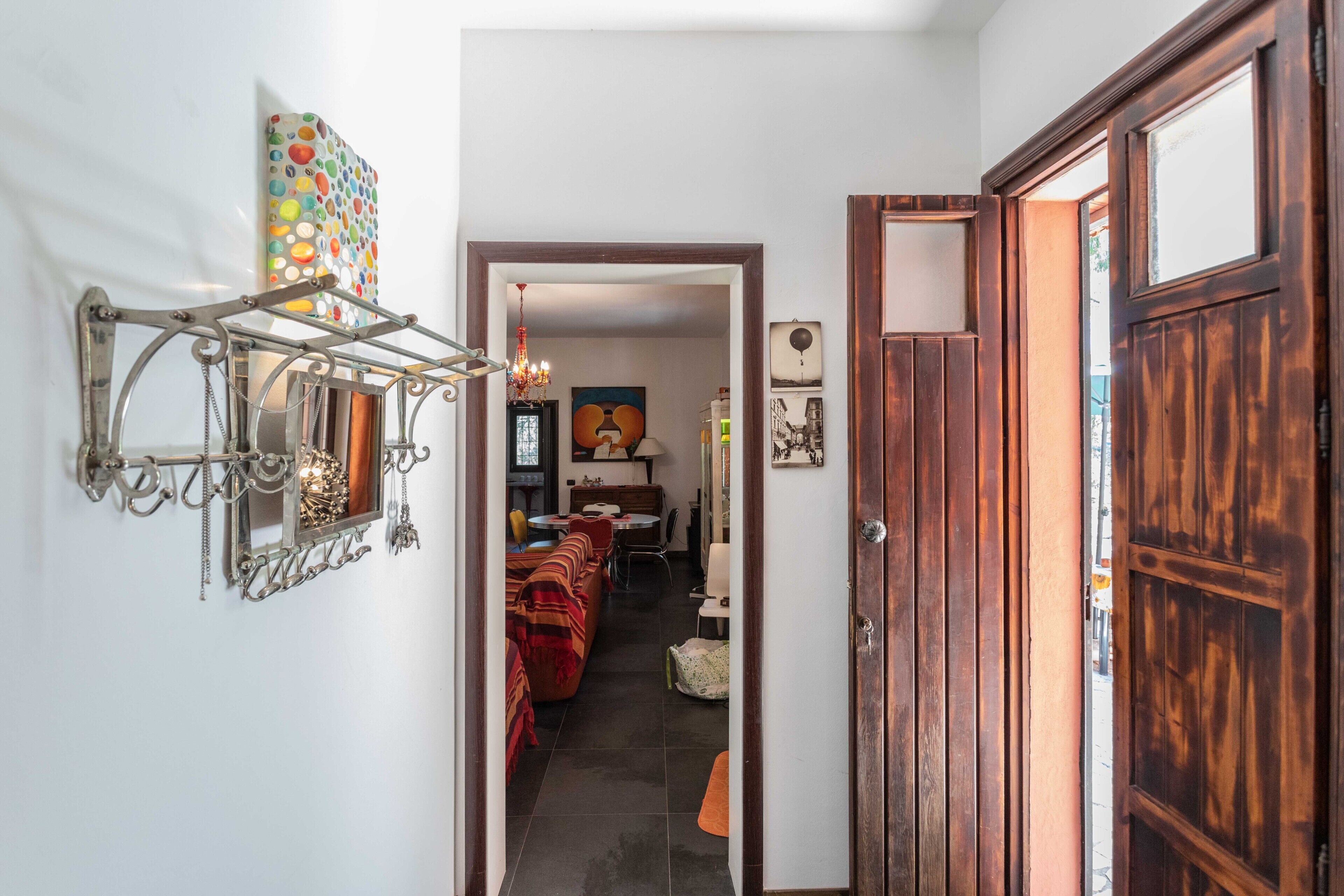 Un couloir avec une porte en bois, un luminaire métallique fixé au mur et une décoration murale colorée.