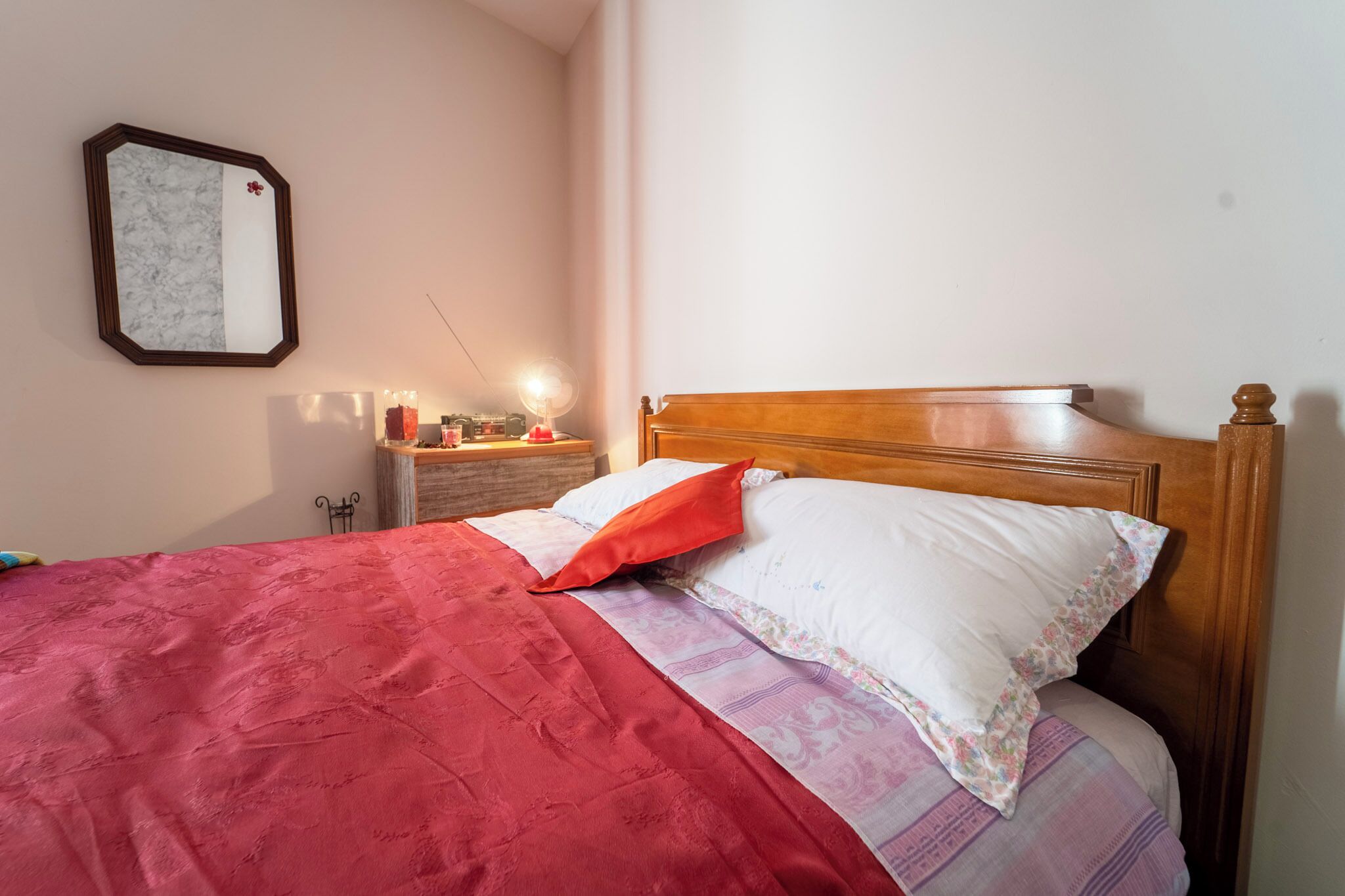 A neatly made bed with a red blanket and a wooden headboard.