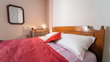 A neatly made bed with a red blanket and a wooden headboard.