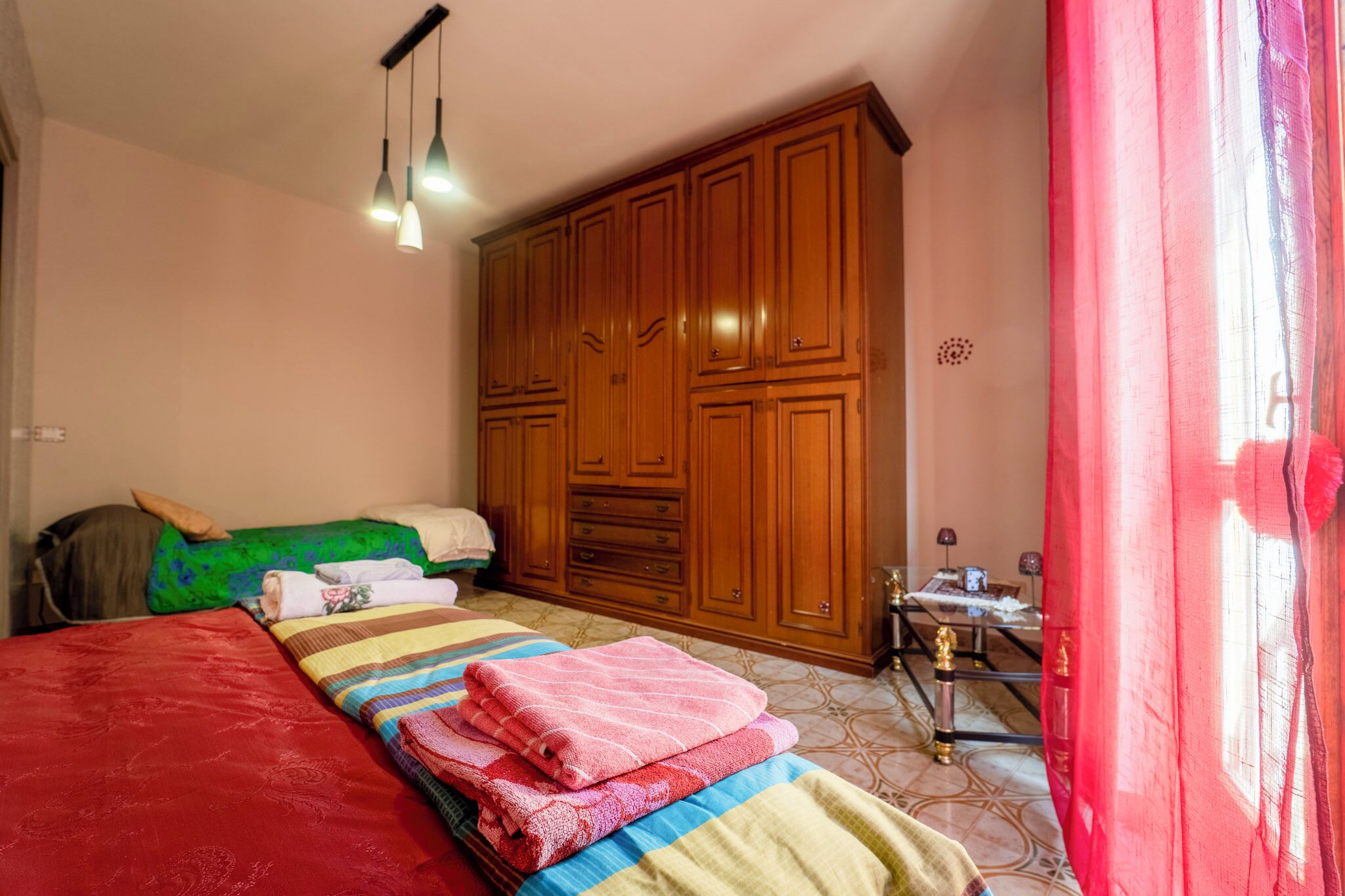 Un dormitorio con cama, armario, escritorio con lámpara y ventana con cortinas.