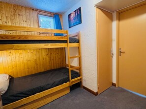 A bunk bed room with a wooden wall, a door, and a window with blue curtains. - Charming studio in the heart of Les Deux Alpes for 4 people (Les Deux Alpes)