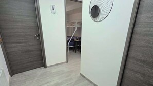 Ein Korridor mit einem Schlafsaal im Hintergrund, einer Tür mit einem 'Plage'-Schild und einer runden Wanddekoration.