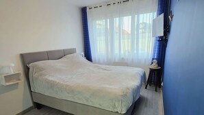Ein Schlafzimmer mit einem Bett, einem Nachttisch, einem Stuhl und einem Fenster mit Vorhängen.