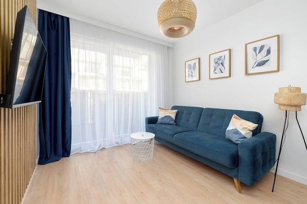 Bright living room with a blue sofa, framed wall art, and large window bringing in natural light.