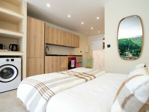 A modern bedroom with a bed, a washing machine, and a mirror reflecting a garden view. - Elegant Garden Suite in Anse Marcel (Saint-Martin)